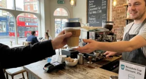 Handing a KeepCup to a barista to claim a reusable cup discount at a UK coffee shop.