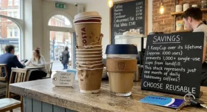 A KeepCup reusable coffee cup next to disposable paper cups to show environmental savings.