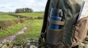 A leakproof travel mug tucked safely into the side pocket of a rucksack during a countryside walk.